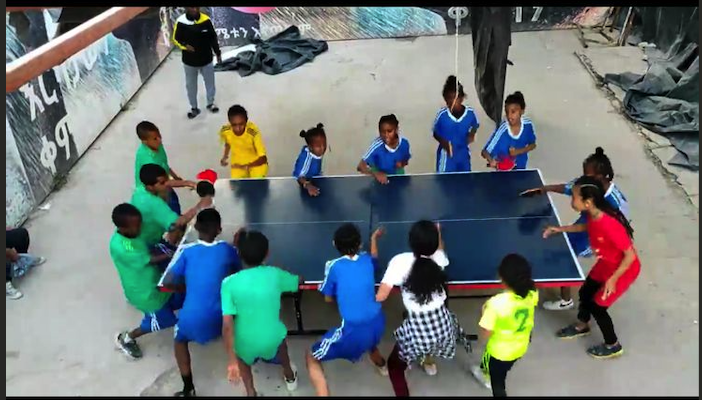 Ethiopian children gathered around a table tennis table playing together outdoors